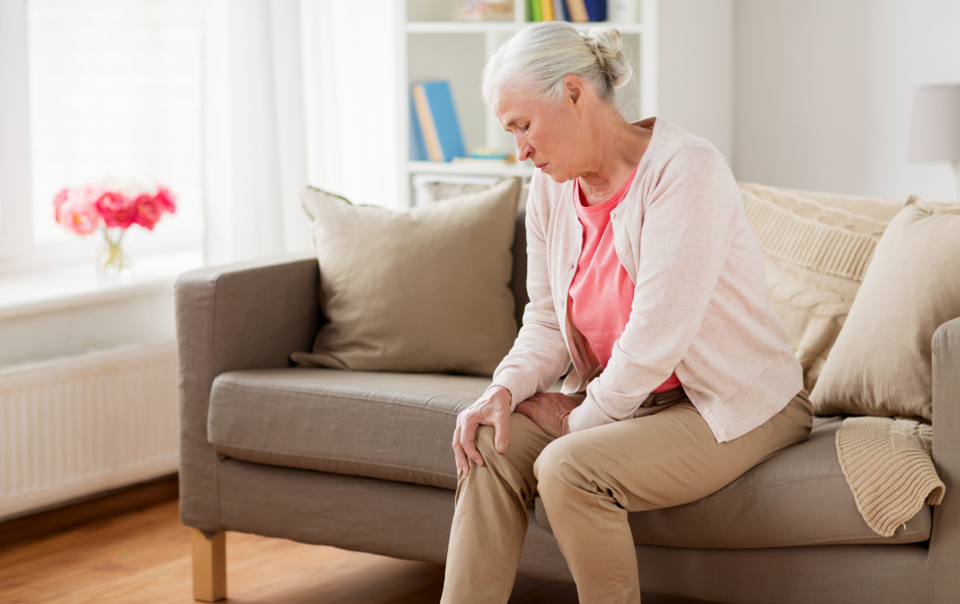 An older woman sitting on her couch massages her arthritic knee that worsens at night.