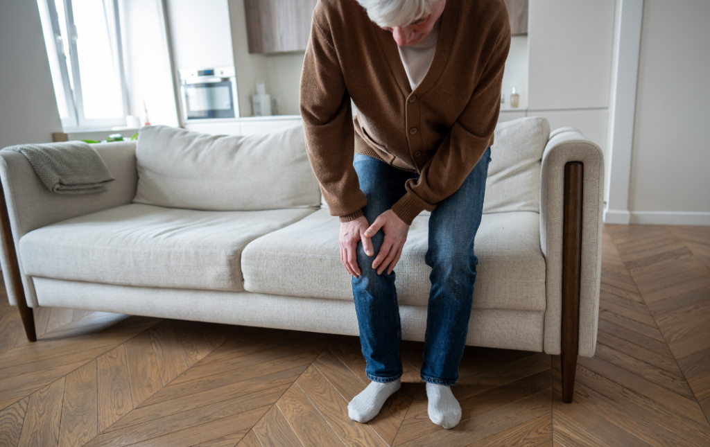 Older man bent over, holding his knee due to pain.