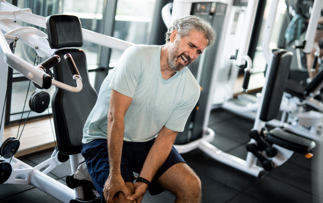 A man holds his knee in extreme pain on the inside of his knee while working out.